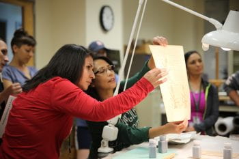 Gloria Garza and Nellie Kvapil (left to right) examine a document while learning about book binding during a tour of the plant and rare book library at the Missouri Botanical Garden’s Monsanto Research Building.